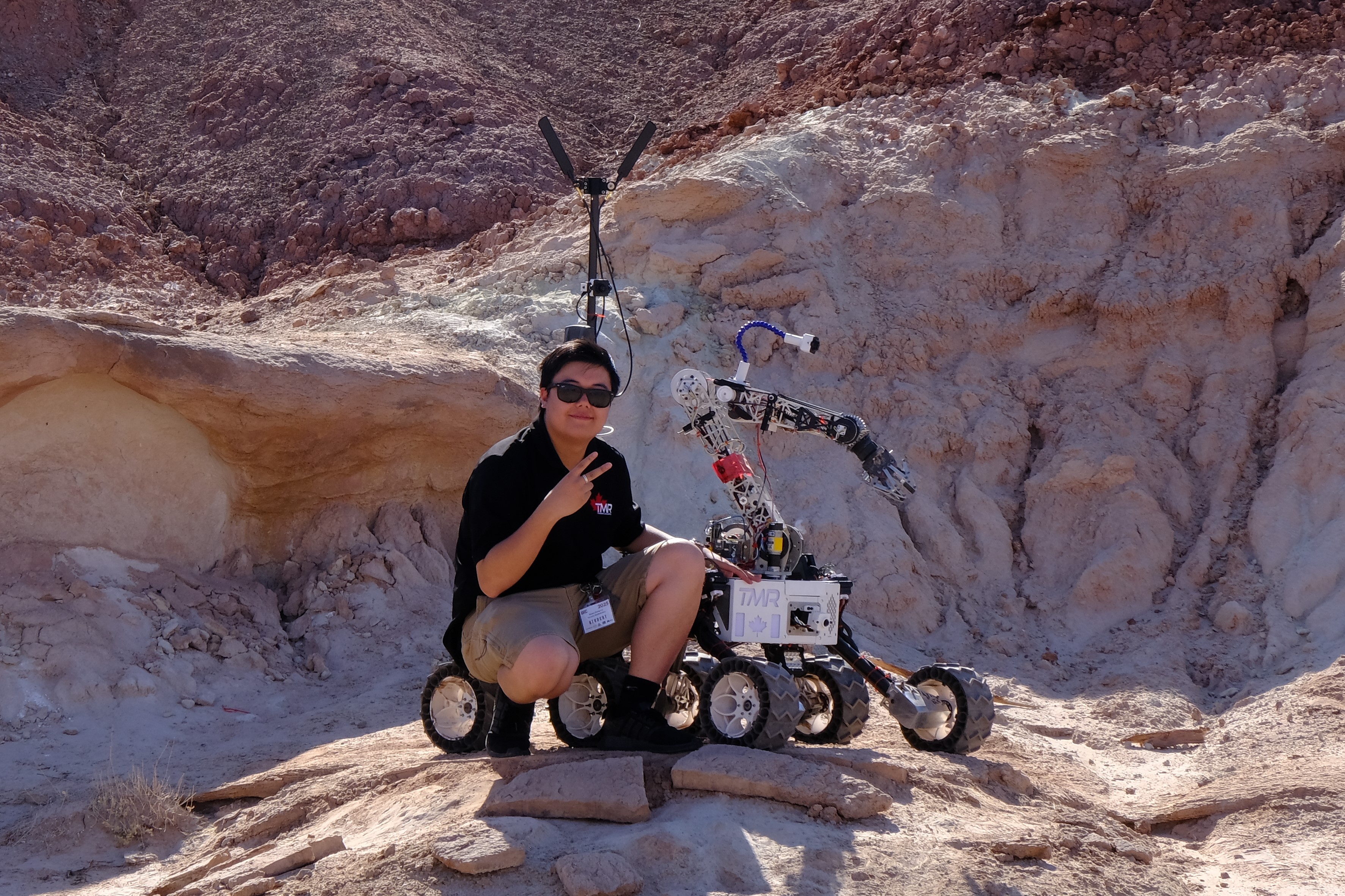 Ryan crouched beside the Toronto MetRobotics rover at University Rover Challenge 2025